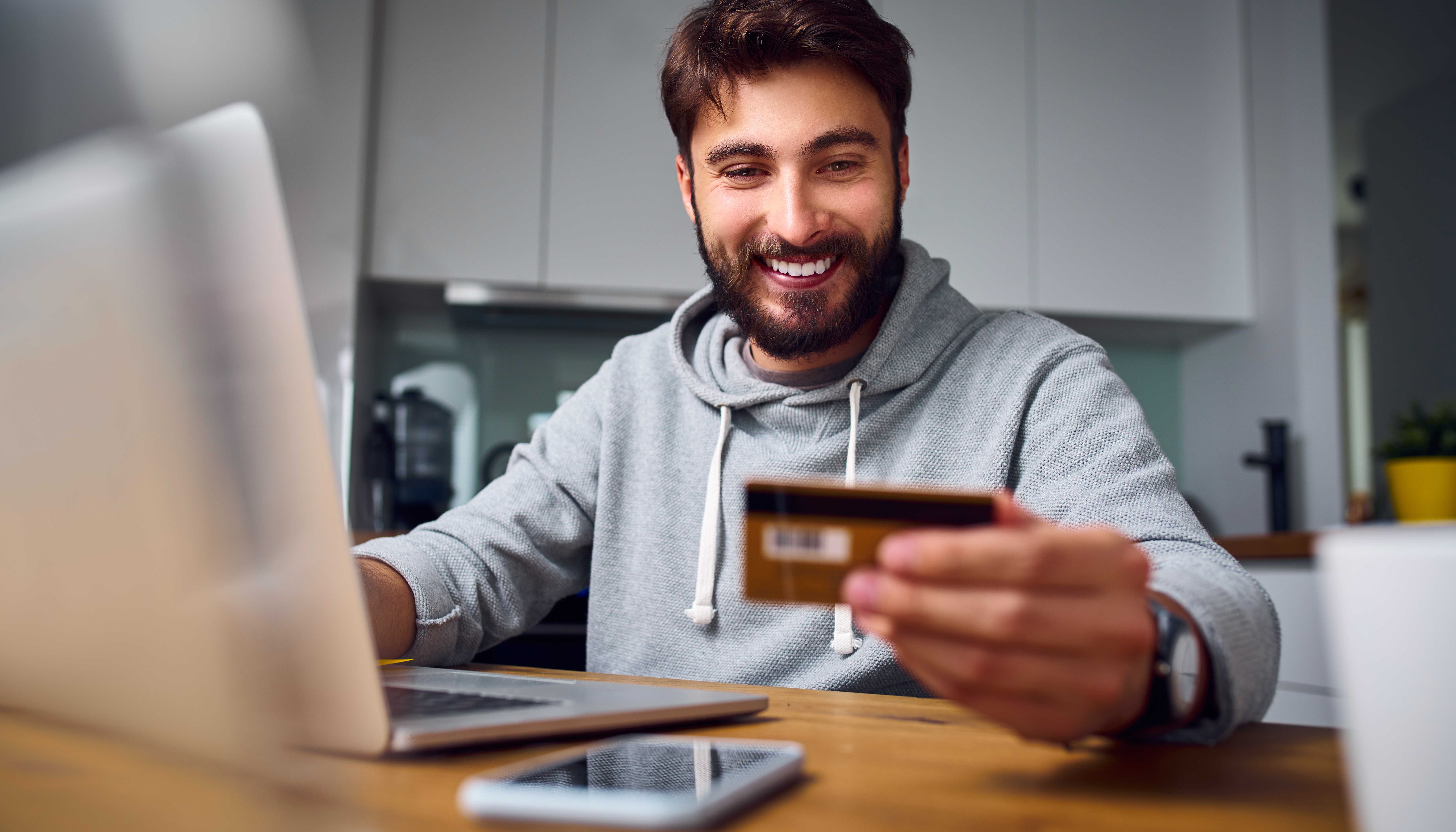 Cheerful young man paying bills online with credit card and laptop